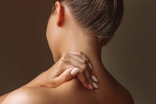 Cropped shot of a young woman standing with her back holds her neck massaging a trapezius muscle with her hand