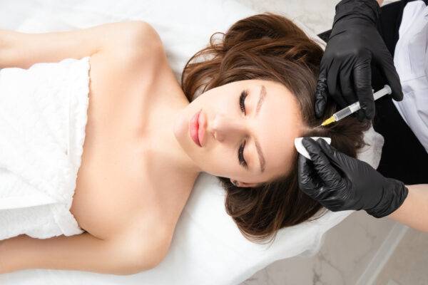 Mesotherapy,  vitamin injections in head skin of hair area. Professional hair loss treatment. Close up view of woman head and doctor's hands with syringe. View above