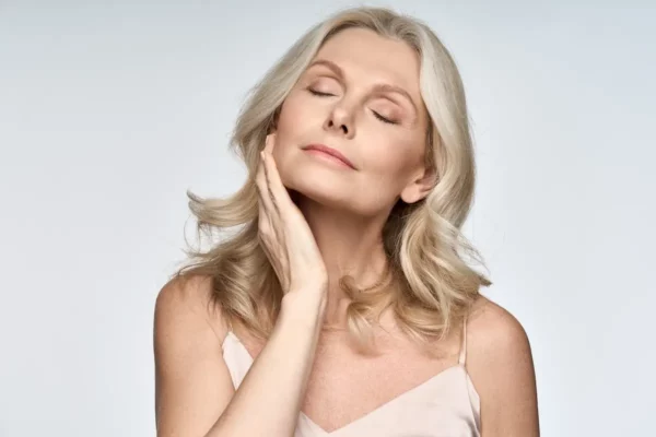 Gorgeous senior older woman with closed eyes touching her perfect skin. Beautiful portrait mid 50s aged woman advertising facial antiage lift products salon care tighten skin isolated on white.